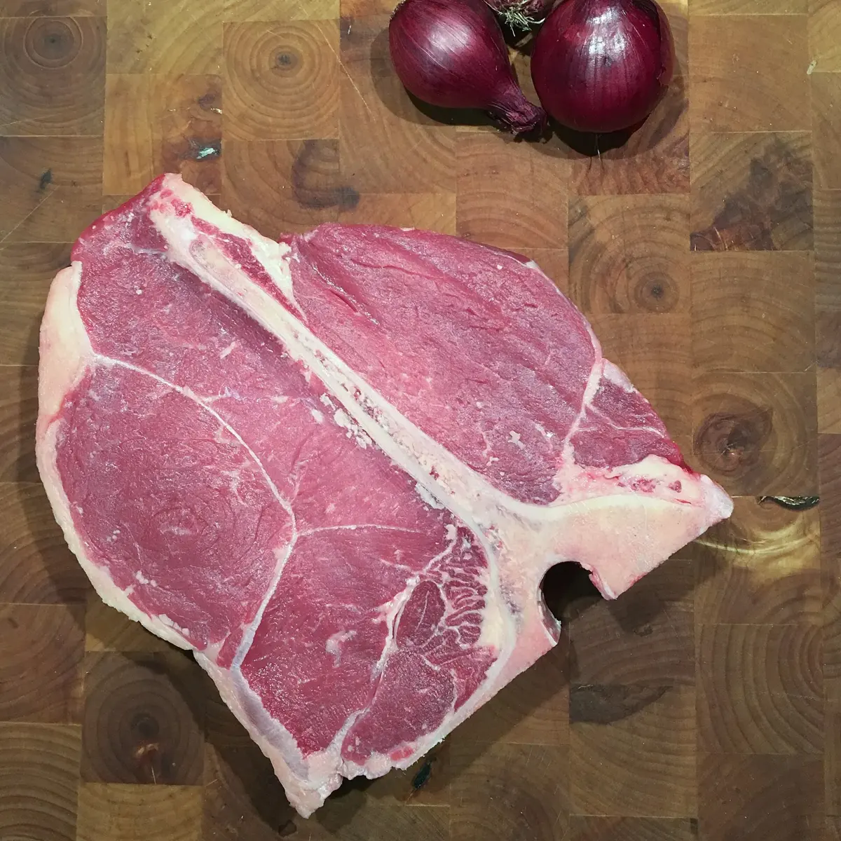 A raw porterhouse steak showing the strip and tenderloin on either side of the bone